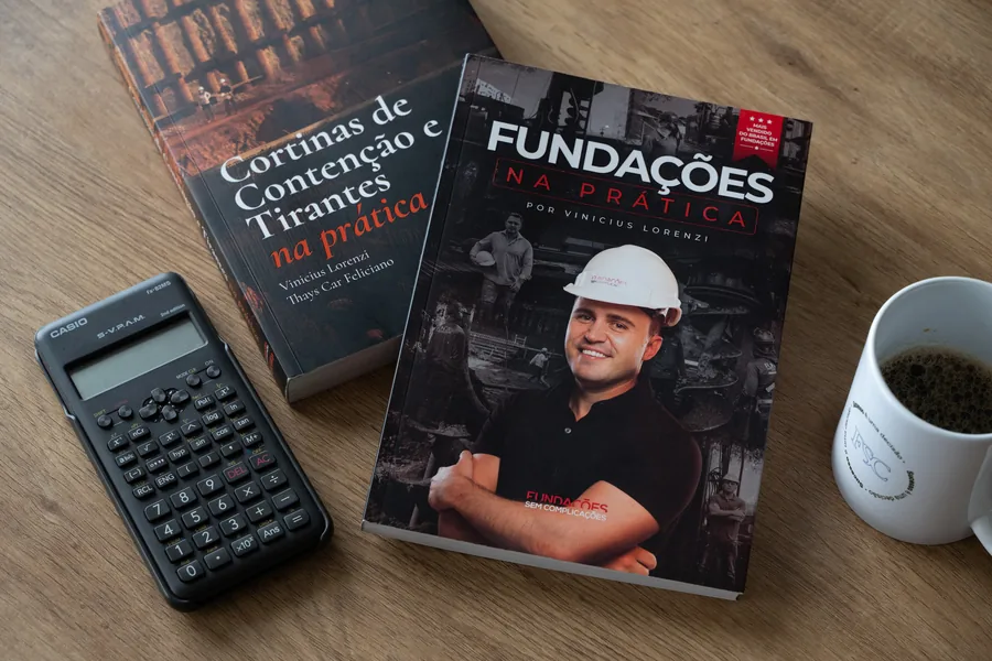 Os livros Fundações na Prática e Cortinas de Contenção e Tirantes na Prática sobre uma mesa, ao lado de uma calculadora científica